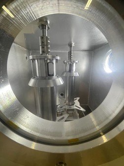 Twin specimen fixtures mounted inside the lit vacuum chamber